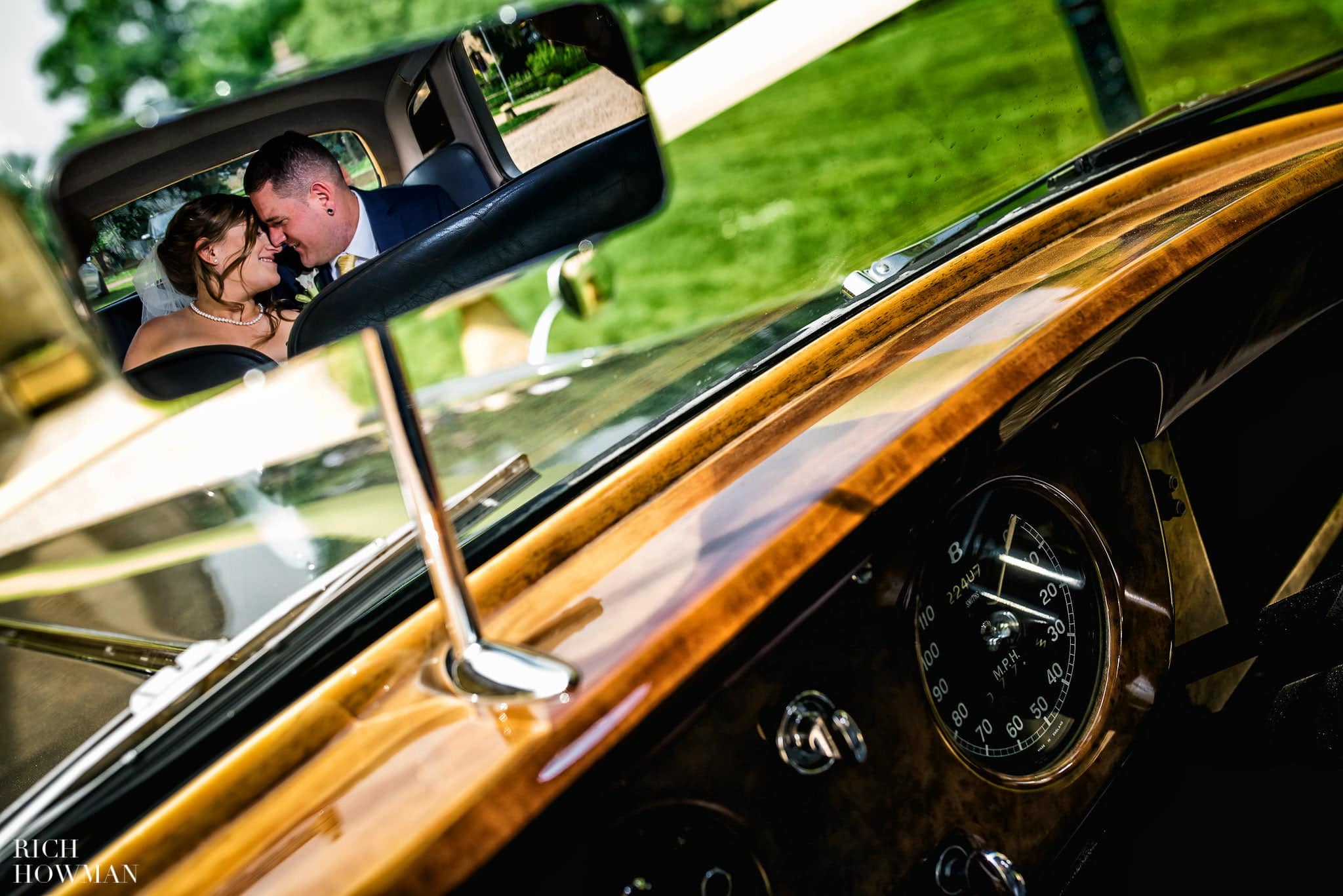 Newly married bride and groom creative portrait, reflected in the rear view mirror of a vintage Bentley