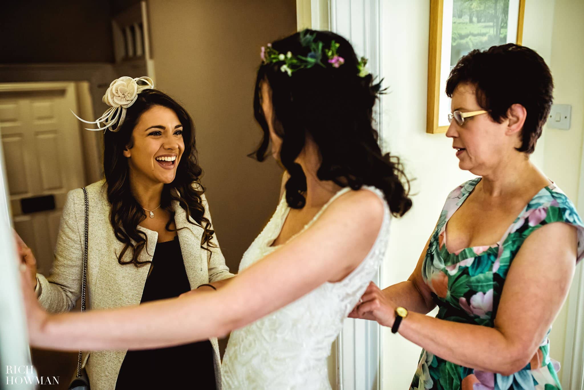 Bridesmaid laughing whilst helping the bride get her dress on