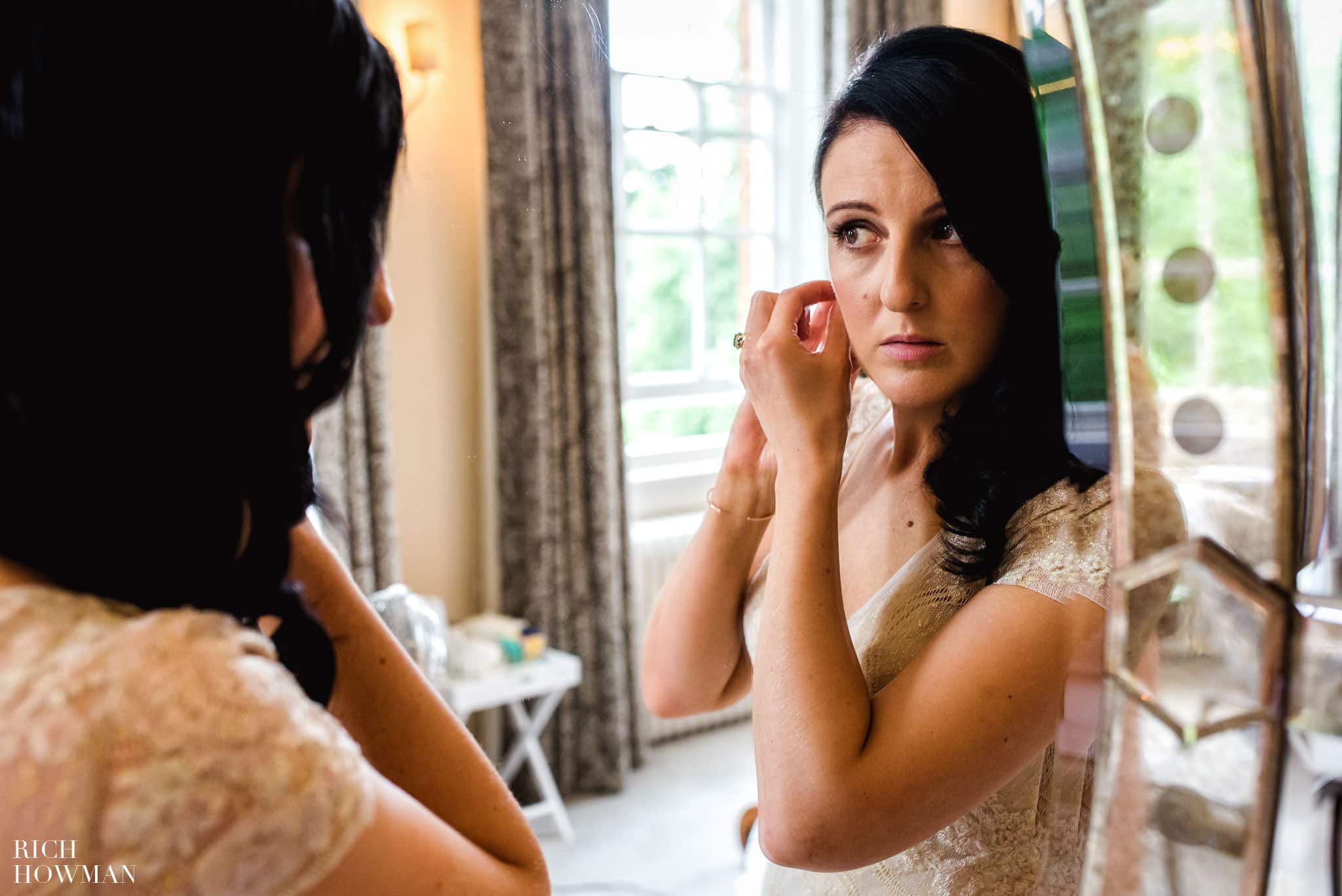 Bride putting on her earrings reflected in a mirror