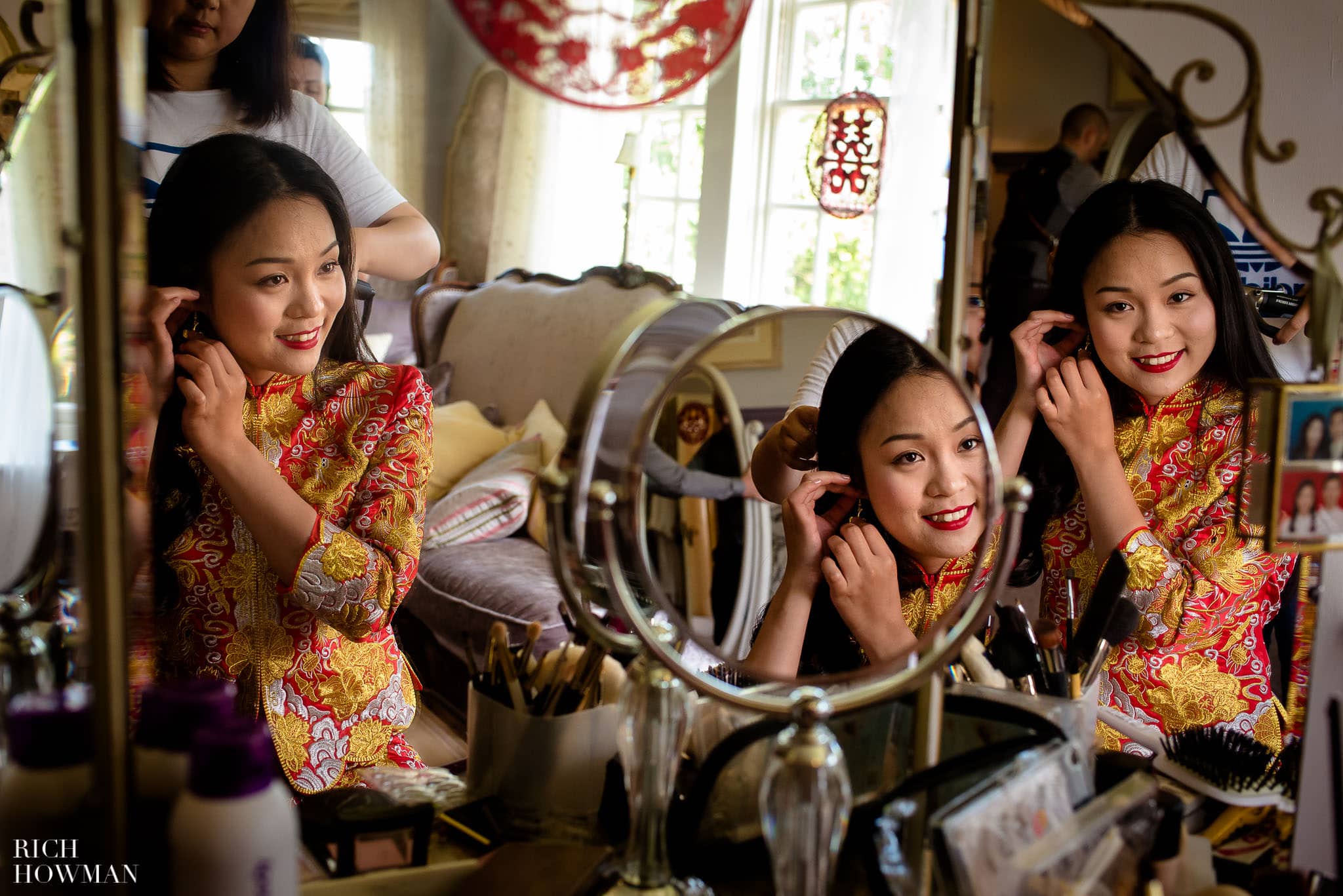Chinese bride reflected in mirrors as she gets ready during her wedding at Brinsop Court