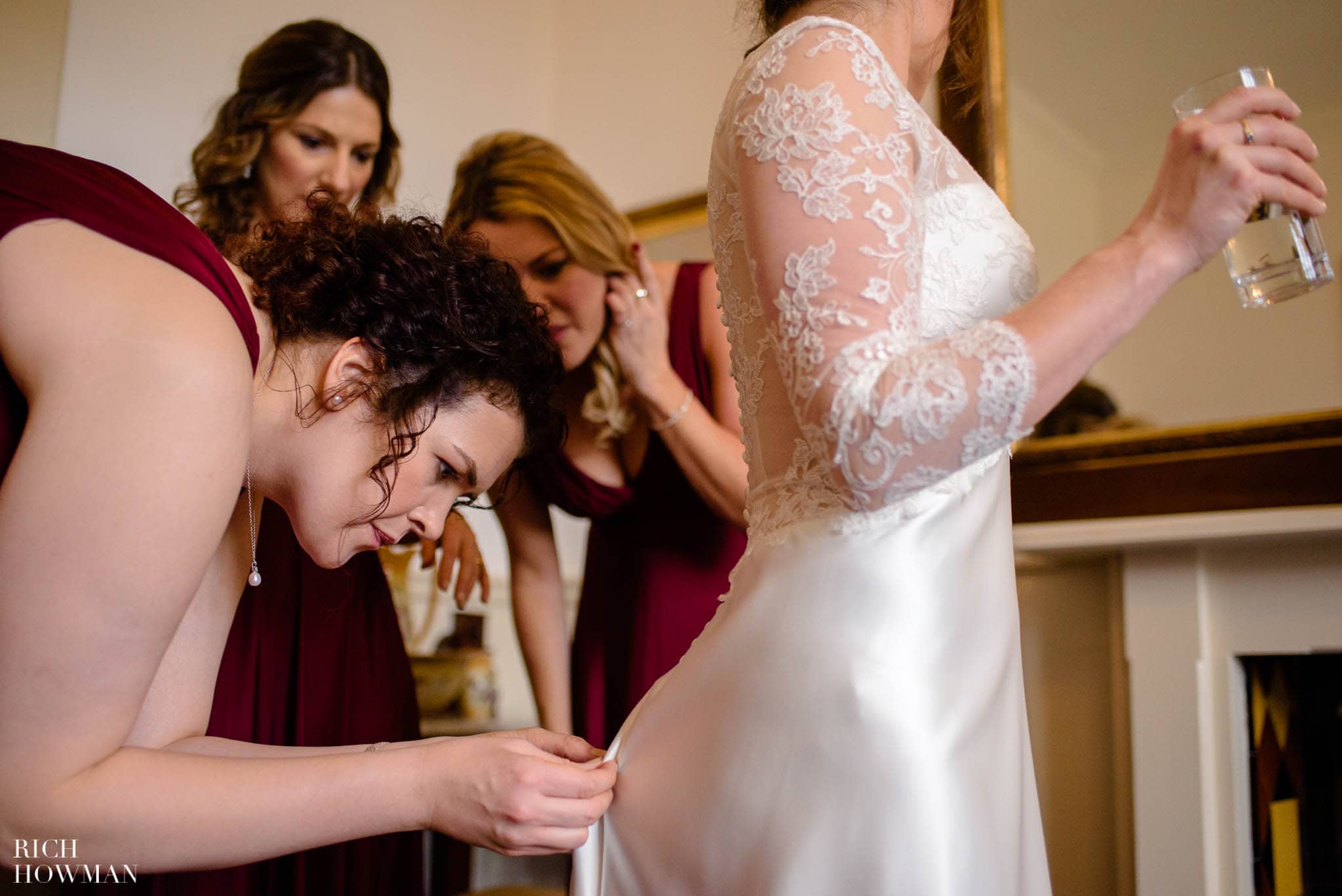 Bridesmaids helping the bride get ready by doing up her wedding dress at the back